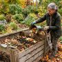 Gardener adding organic kitchen scraps to a wooden backyard compost bin.